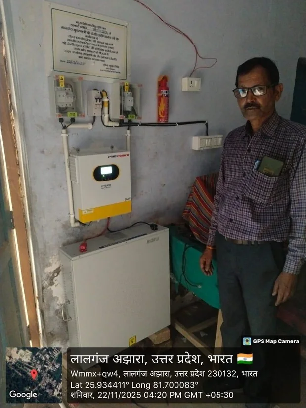 Wall-mounted hybrid solar inverter and floor-standing LFP battery enclosure with commissioning plaque, installed at a cooperative building in Lalganj Ajhara, Uttar Pradesh
